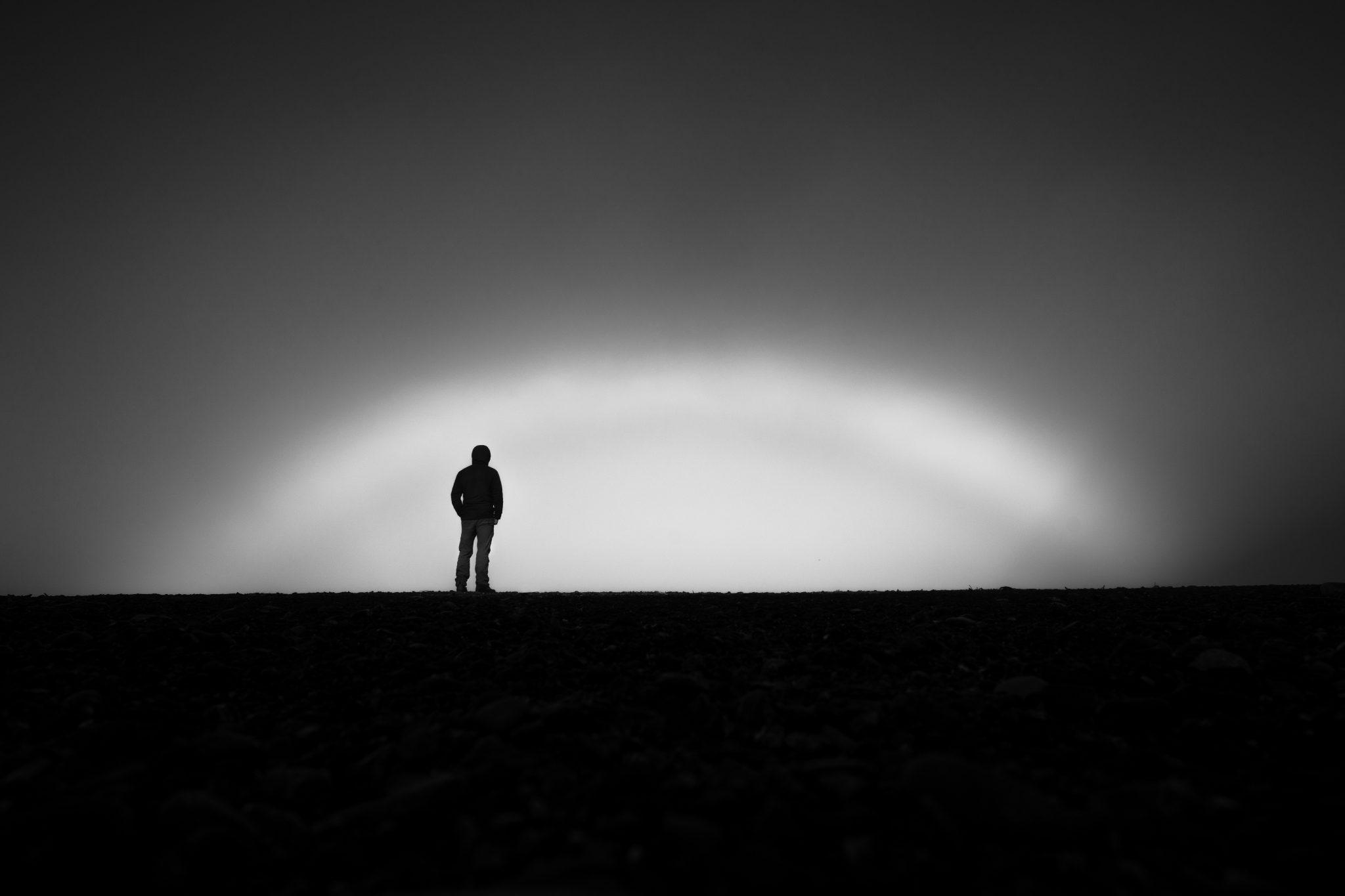 Black and white photo of man standing on a hill with sun coming up at dawn.