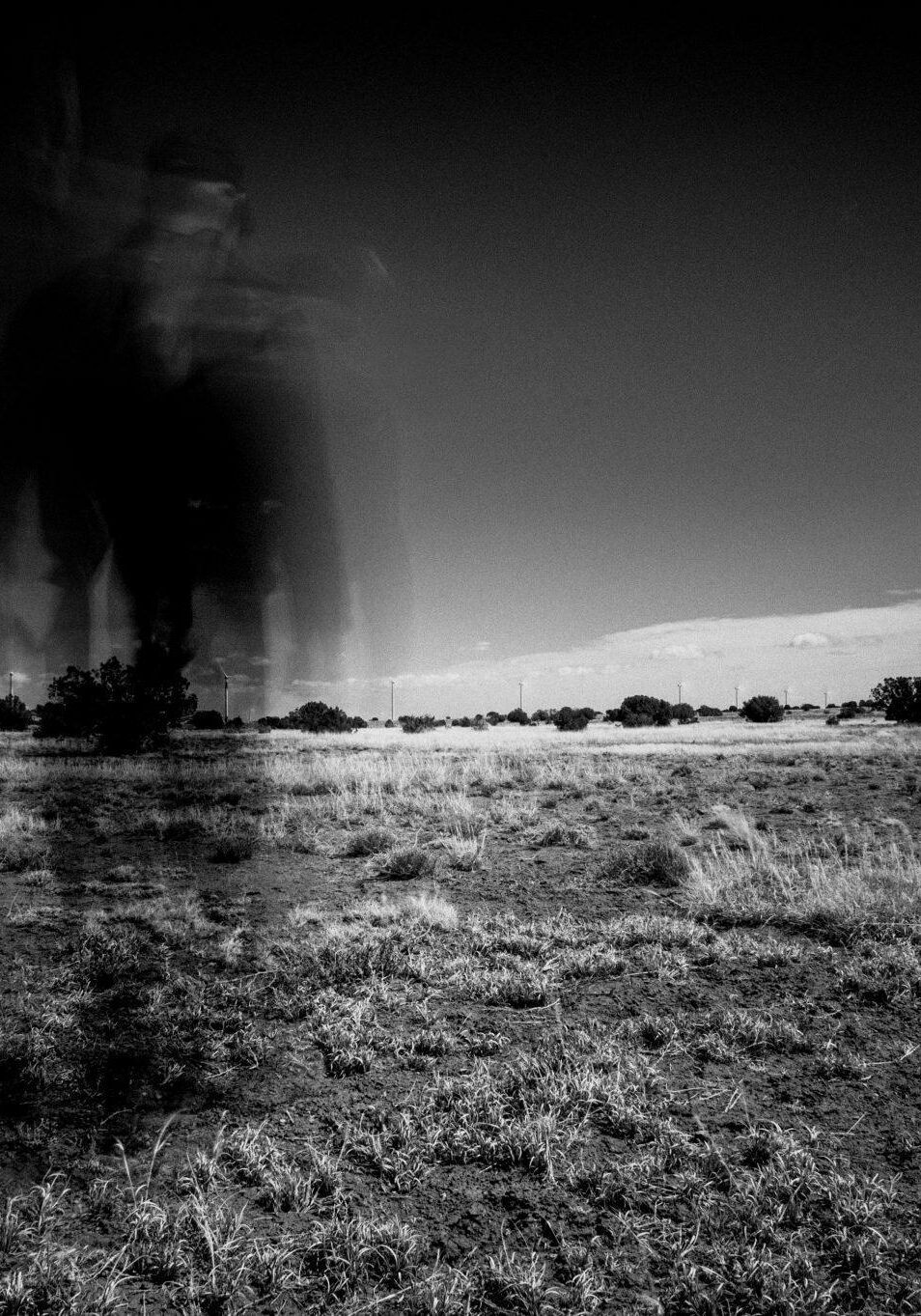 Black and white photo of a man blurred, walking through a field.